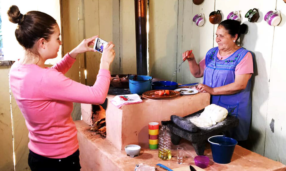 Doña Ángela grabando una receta para su canal "De mi Rancho a tu Cocina" con ayuda de su hija